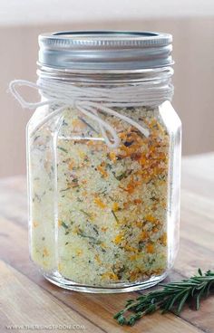 a jar filled with herbs sitting on top of a wooden table next to a sprig of rosemary