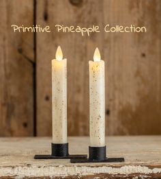 two white candles sitting next to each other on top of a wooden table with the words primitive pineapple collection written above them