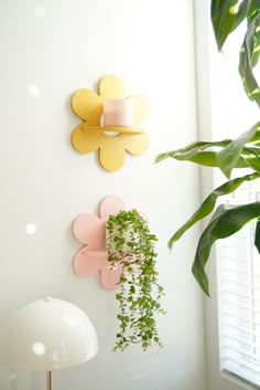 three flower shaped wall hangings on the wall next to a lamp and potted plant