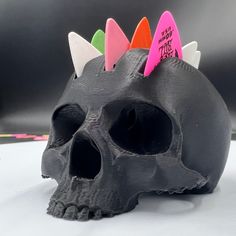 a black skull with colorful spikes on it's head sitting on a white surface