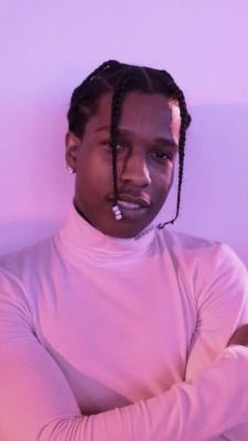 a man with dreadlocks standing in front of a pink wall wearing a white shirt