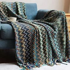 a blue couch with a blanket on top of it and a cup in the middle