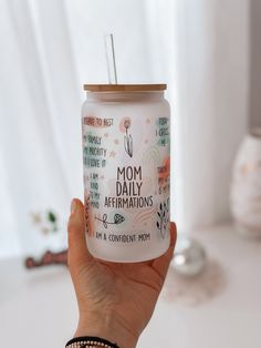 a person holding up a glass with the words mom daily affirmations on it