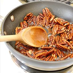 the pecans are being cooked in the pan on the stove top with a wooden spoon