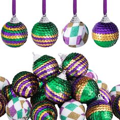 several different colored christmas ornaments hanging from purple and green corded balls on white background