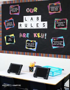 a classroom desk with laptops on it and a blackboard in the background that says our lab rules are keu