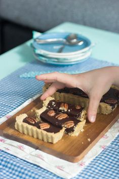 a person reaching for a piece of food on a wooden cutting board at a table