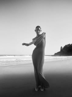 a woman standing on top of a beach next to the ocean wearing a long dress