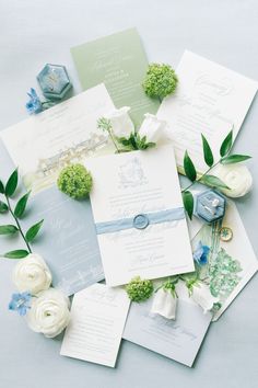 the wedding stationery is laid out on top of each other with flowers and greenery