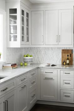 a kitchen with white cabinetry and marble counter tops, along with green apples in a bowl