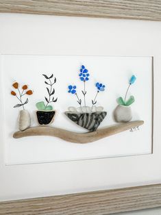 some rocks and flowers are sitting on a wooden branch in front of a white frame