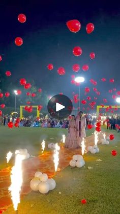 two people standing in the middle of a field surrounded by red and white balloons