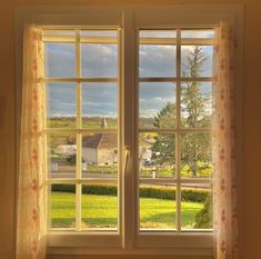 two windows with curtains open in front of a green yard and houses outside the window