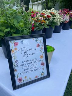 there is a sign on the table that says flower box and flowers in pots behind it