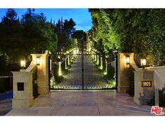 an entrance to a home with lights on the gate and trees in the background at night