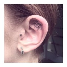 a woman's ear with an arrow and leaf tattoo on the left side of her ear