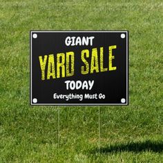 a yard sale sign sitting on top of a lush green grass covered field next to a black and white sign that says, giant yard sale today everything must go