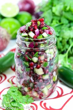 a mason jar filled with cucumber salsa surrounded by fresh vegetables and cilantro