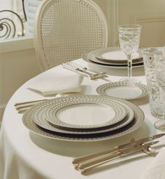 the table is set with silver and white plates, silver cutlery, and glasses