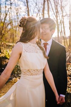 a bride and groom holding hands in the woods at their wedding day with sunlight streaming through the trees behind them