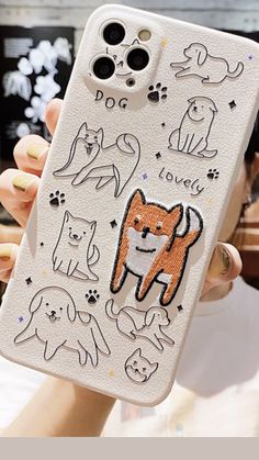 a woman holding up a phone case with dogs and cats drawn on the back of it