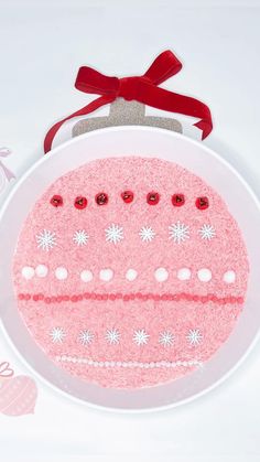 a pink cake on a white plate with snowflakes and red ribbon around it