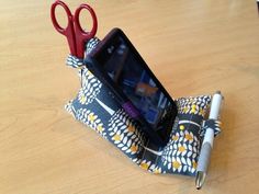 a cell phone sitting in a holder on top of a wooden table next to a pen and scissors