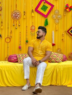 a man sitting on a bed in front of a yellow wall covered with jewelry and decorations