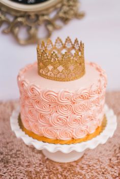 there is a pink cake with a gold crown on top that is sitting on a table