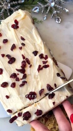 someone cutting into a cake with white frosting and cranberries