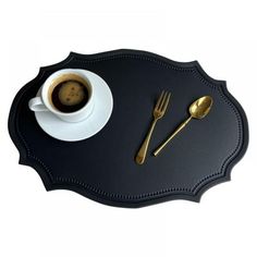 there is a cup of coffee and two spoons on the black tray with gold trim