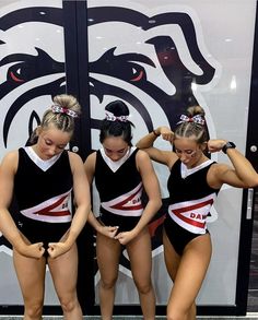 three girls in black and white cheerleader outfits standing next to each other with their hands on their hips