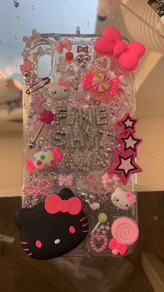 an iphone case with hello kitty and other items on it, sitting in front of a window