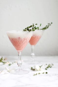 two glasses filled with pink liquid and garnished with greenery