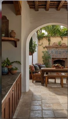 an archway leading to a patio with seating and fireplace in the center, surrounded by potted plants