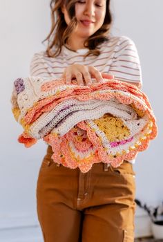 a woman is holding a pile of crocheted blankets