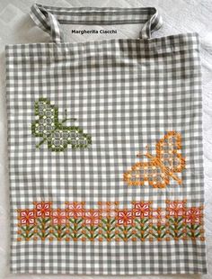 an embroidered shopping bag sitting on top of a white table cloth covered in checkered fabric