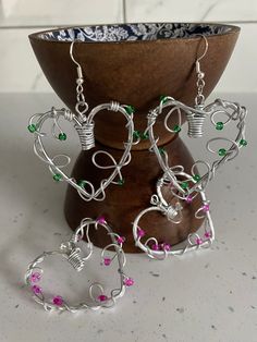 a pair of heart shaped earrings with pink and green beads on them sitting in front of a vase