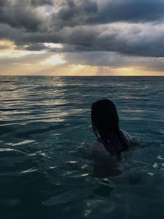 a woman swimming in the ocean under a cloudy sky