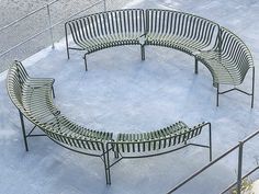 four benches are arranged in a circle on the concrete flooring area, with metal railings around them