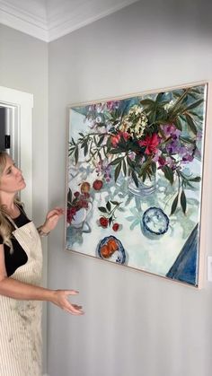 a woman in an apron pointing at a painting on the wall