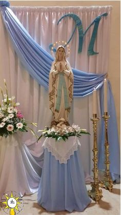 a statue of the virgin mary in front of a blue and white backdrop with flowers