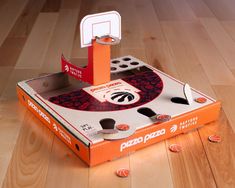 an unopened pizza box with a basketball hoop in it on a wooden floor