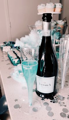 a bottle of champagne next to some glasses on a table with confetti and cupcakes