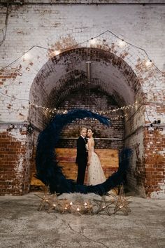 a bride and groom standing in front of an arch with lights on the wall behind them