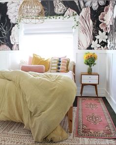 a bed sitting in a bedroom next to a window filled with flowers and blankets on top of it