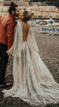 a bride and groom kissing on the beach in front of some buildings with their backs to each other