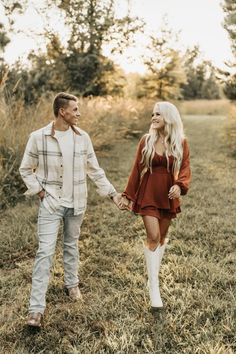 a man and woman holding hands while walking through the grass