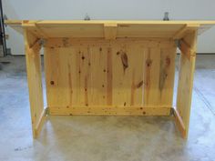 a table made out of wooden planks in a room with concrete flooring and white walls