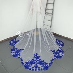 a wedding dress with blue flowers on the bottom and veil hanging from it's side